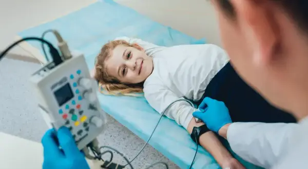 Uśmiechnięta dziewczynka leży na łóżku podczas badania EEG, które pomaga diagnozować padaczkę u dzieci.