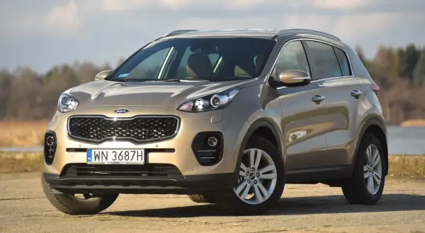 Złoty Kia Sportage na tle jeziora. Sprawdź jego wymiary i możliwości terenowe.