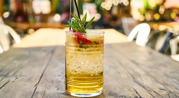 Orzeźwiający drink z marakują, lodem i gałązką rozmarynu na drewnianym stole.