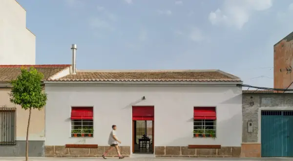 Fachada casa pueblo moderna con persianas rojas vibrantes y un hombre corriendo.