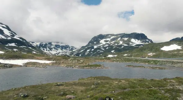 Vacker vy över Hardangervidda med snöklädda berg, en sjö och en väg. Perfekt för en vandring.