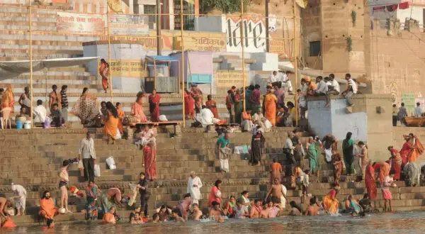 Tłum ludzi w barwnych strojach kąpie się i odpoczywa na schodach nad rzeką Ganges.