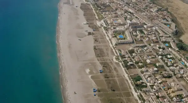 Vista aérea de la playa Las Marinas Vera, con el mar turquesa, arena dorada y un complejo residencial con piscinas.