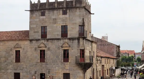 Plaza de Cambados que ver: torre medieval de piedra, casas históricas y gente paseando.