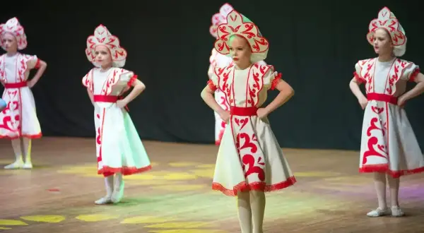 Niñas con trajes tradicionales bailan en un escenario de teatro.