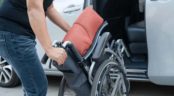 Persona piega una carrozzina vicino a un'auto, pensando all'assicurazione auto legge 104.