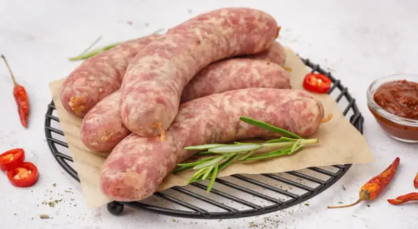 Surowa biała kiełbasa na ruszcie, gotowa do przygotowania. Obok papryczki chili i sos. Idealna do gotowania.