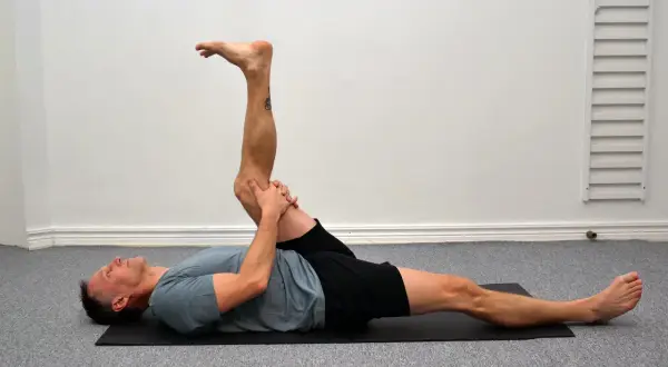 Man utför en leg curl svenska på en yogamatta, sträcker ut ena benet och böjer det andra.