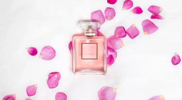 Perfumy Chanel Coco Mademoiselle w różowym flakonie otoczone płatkami róż na białym tle.