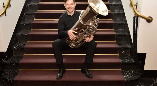 Ein Mann sitzt auf einer Treppe mit einer Tuba. Wer hat die Tuba erfunden? Diese Frage beschäftigt Musiker seit langem.