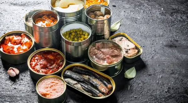 Variedad de latas abiertas con comida supervivencia: guisantes, champiñones, sardinas, carne y más.