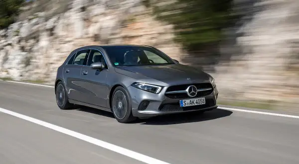 Une Mercedes-Benz Classe A grise roule sur une route de campagne, le paysage flou par la vitesse. Son moteur classe a offre une conduite dynamique.