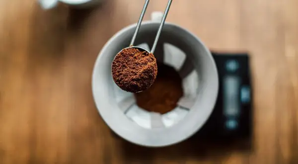 En skopa finmalet kaffe hälls ner i en filterhållare. Perfekt för att mäta rätt mängd gram kaffe per liter vatten för en balanserad bryggning.