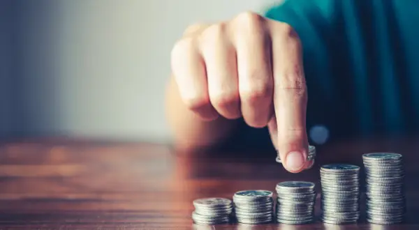 Mano che aggiunge una moneta a una pila, simboleggiando la crescita finanziaria, il risparmio o la gestione del **tutore e indennità di accompagnamento**.