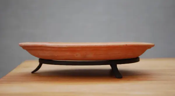 En terrakotta kruka, en av de stora krukfat, står på ett svart metallstativ på ett träbord.