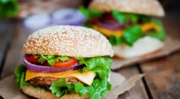 Dwa soczyste burgery z domowym fast foodem, pełne świeżych warzyw i sera, na drewnianym stole.