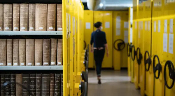 Rayons de livres anciens dans les archives départementales d'Indre-et-Loire en ligne, une personne se déplace dans l'allée.