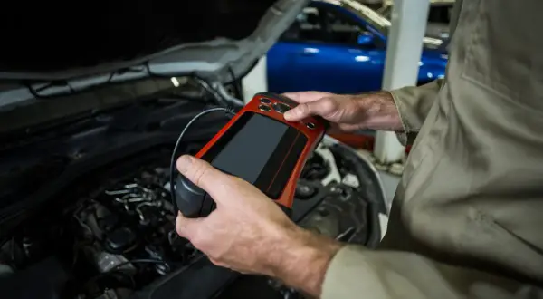 Mechanik z urządzeniem diagnostycznym przy silniku. Czy odłączenie akumulatora na chwilę pomoże zresetować komputer?