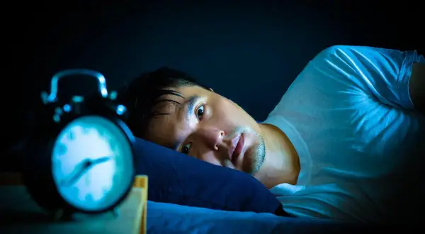 Hombre en cama, con ojos abiertos y alarma. Podría estar experimentando alucinaciones hipnagógicas.