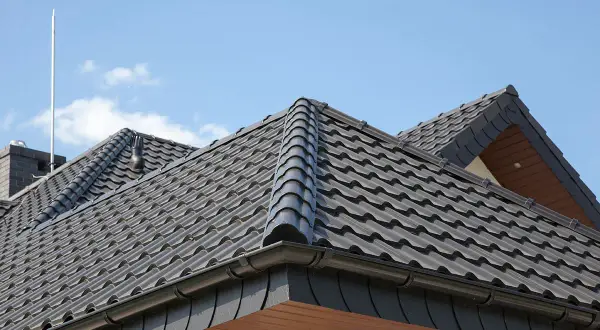 Szary dach czterospadowy z dachówki ceramicznej, z widocznym kominem i piorunochronem.