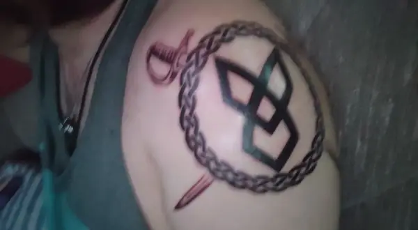 Tatuaż na ramieniu: symbol odrodzenia, spleciony łańcuch, szabla i sztylet.