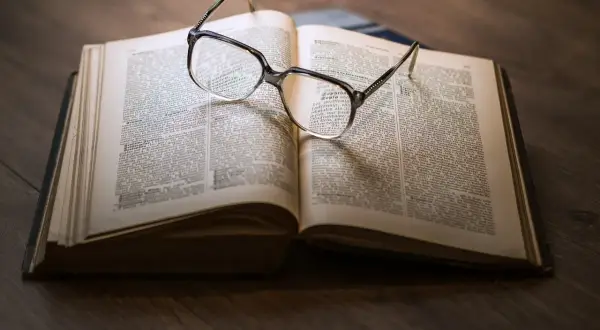Eine Brille liegt auf einem aufgeschlagenen Buch mit informierenden Texten.