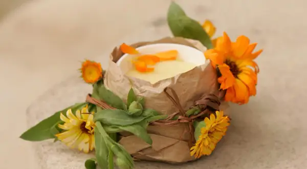 Selbstgemachte Ringelblumensalbe in einem Becher, verziert mit frischen Ringelblumen und Blättern.