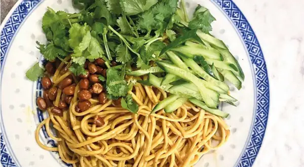 En läcker asiatisk nudelsallad med krispig gurka, rostade jordnötter och färsk koriander på en vackert mönstrad tallrik.