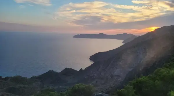 Atardecer en el mirador del Roldán, con el mar Mediterráneo y montañas escarpadas bajo un cielo de nubes rosadas y anaranjadas.