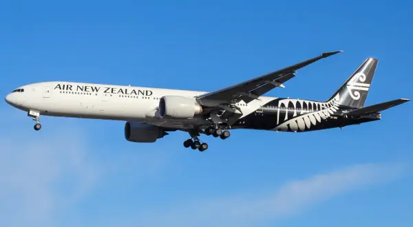 Boeing 777 Air New Zealand z charakterystycznym czarnym malowaniem na ogonie, w locie na tle błękitnego nieba.