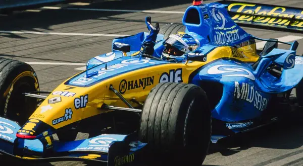 Un coche de Renault F1 azul y amarillo, con el piloto saludando.