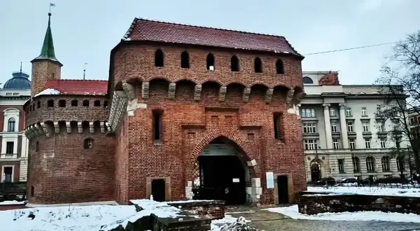 Imponujący barbakan kraków z cegły, z charakterystycznymi łukami i blankami, otoczony zimowym krajobrazem.