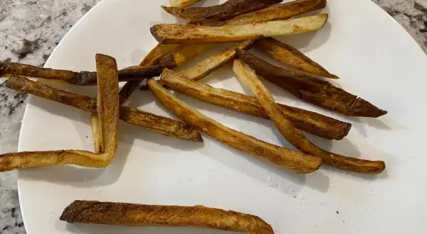En tallrik med krispiga pommes frites, perfekt tillagade i airfryer. Saltkorn glittrar på de gyllene pommes.