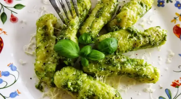 Pyszne gnocchi z pesto, posypane parmezanem i udekorowane listkami bazylii. Widok na talerzu z kolorowym wzorem.