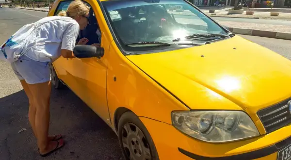 Kobieta pyta kierowcę żółtej taksówki, czy w Tunezji można płacić euro.