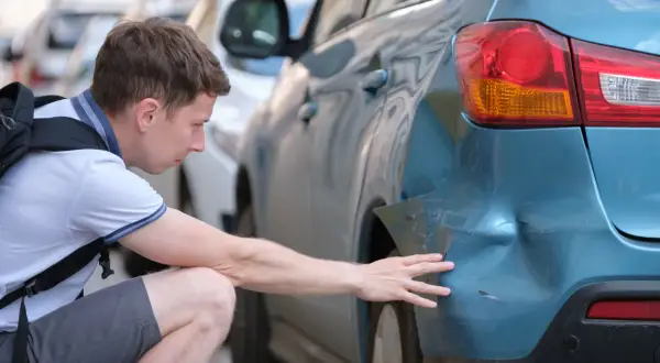 Mann untersucht Delle am blauen Auto. Hoffentlich keine Geisterfahrer-Strafe wegen des Schadens.