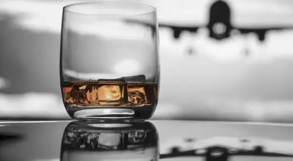 Szklanka whisky z lodem na tle samolotu. Czy można przewozić alkohol w samolocie Ryanair?