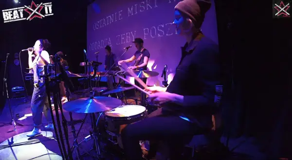 Wiktoria Jakubowska na perkusji, w rytmie muzyki, z pałeczkami w dłoniach, tworzy energię na scenie.