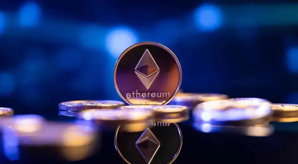 Eine glänzende Ethereum-Münze, die das Symbol und den Namen trägt, steht im Fokus. Sie ist Teil einer Ansammlung von Münzen, die auf einer dunklen, spiegelnden Oberfläche liegen und die Zukunft von eth 2.0 symbolisieren.