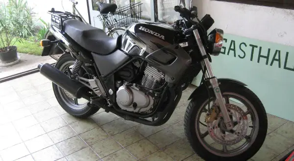 Czarny motocykl Honda z widocznym silnikiem i wydechem, gotowy do jazdy. Obok stoi rower.