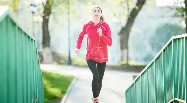 Une jeune femme en tenue de sport court sur un chemin bordé de verdure. Elle semble apprécier son activité, peut-être pour courir 20 minutes par jour.