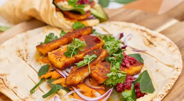 En läcker halloumi wrap med hummus, rivna morötter, rödlök och färska örter. En annan wrap syns i bakgrunden.