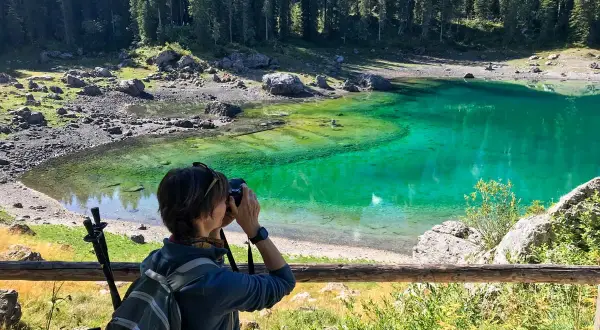 Donna con zaino e macchina fotografica cattura la bellezza del Lago di Carezza, un luogo imperdibile tra le meraviglie del Trentino Alto Adige cosa vedere.