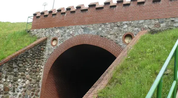 Akwedukt w Fojutowie, z ceglanym łukiem i kamiennym murem, otoczony zielenią.