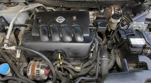 Silnik Nissan Qashqai J10, widok z góry. Czarna pokrywa silnika z logo Nissan, alternator, akumulator i przewody.