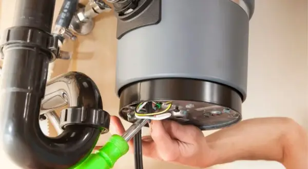 A person is working on a garbage disposal that is not working, connecting wires with a screwdriver.