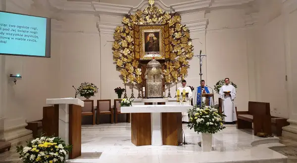 Msza w kościele w Dąbrówce Kościelnej. Trzech duchownych przy ołtarzu, ozdobionym złotym antepedium i obrazem Matki Boskiej.