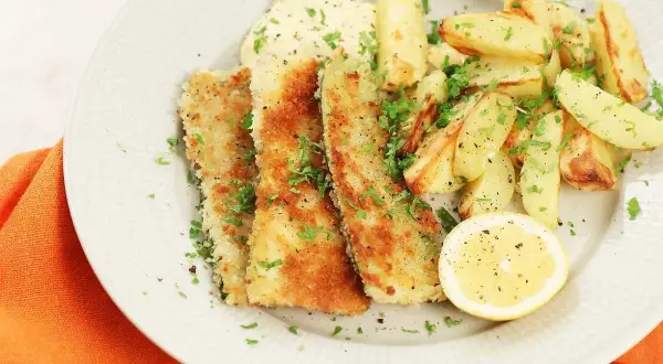 Krispiga bitar av pankopanerad zucchini serveras med ugnsrostade potatisklyftor, en klick sås och en citronskiva.