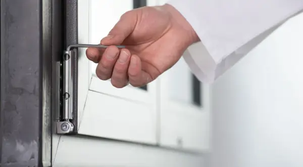 Dłoń z kluczem imbusowym reguluje zawias okna. Przygotowanie do trybu zimowego regulacja okien na zimę.