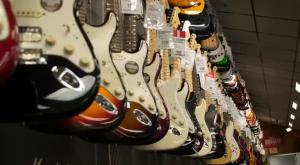 Rząd gitar elektrycznych w sklepie. Widać różne kolory i modele, w tym pierwsza gitara elektryczna z pięknym wykończeniem.